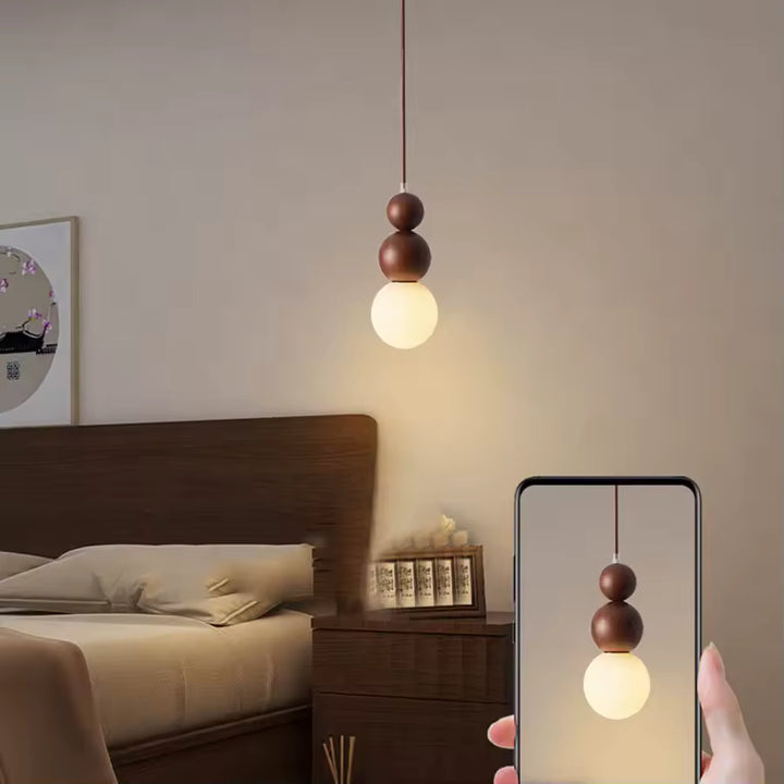 Suspension totem en bois à globe opalin près du lit, dans une chambre chaleureuse au style minimaliste et naturel