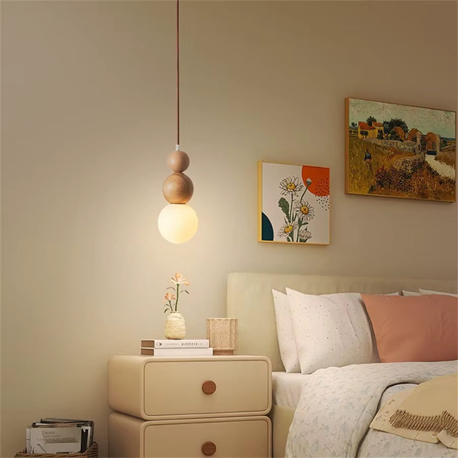 Suspension totem en bois clair à globe opalin près du lit, dans une chambre douce au style japandi et chaleureux