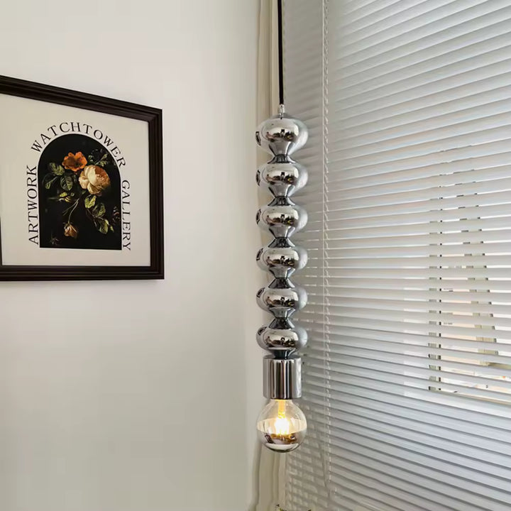 Présentée près d’une fenêtre, cette suspension totem chromée à ampoule filament mêle design sculptural et style contemporain