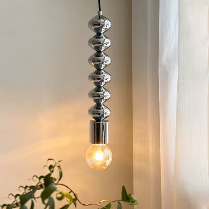 Éclairage chaleureux sous une suspension totem chromée à ampoule filament, au style contemporain et sculptural