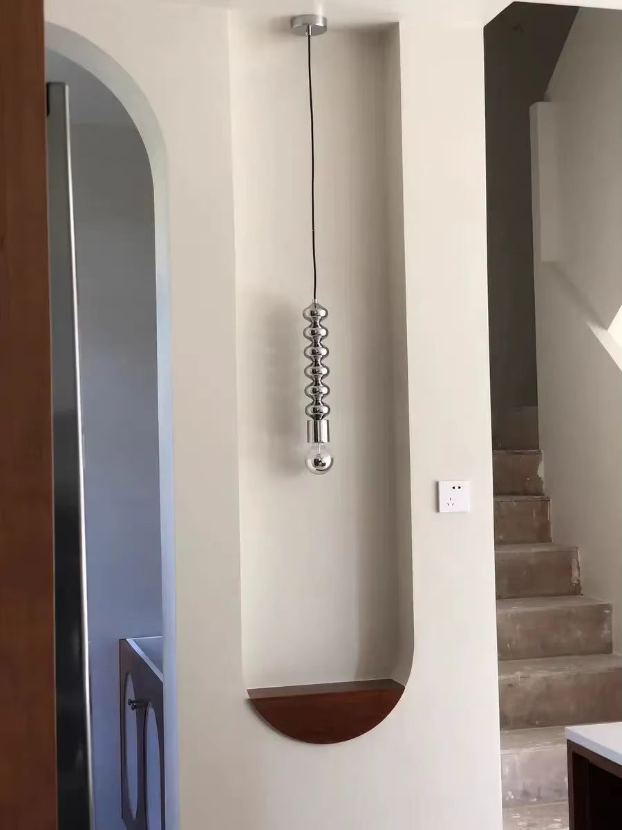 Dans une entrée épurée, cette suspension totem chromée affirme un style minimaliste, contemporain et sculptural