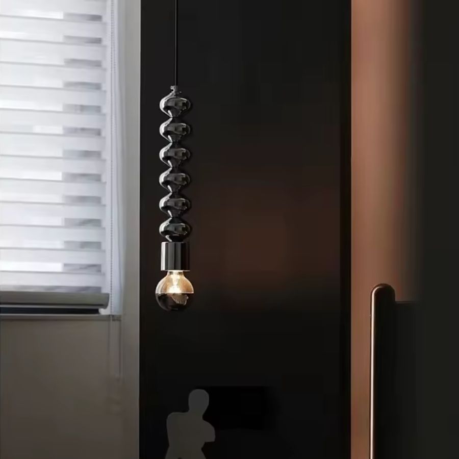 Ambiance graphique autour d’une suspension totem en métal noir à ampoule métallisée, au style contemporain et sculptural