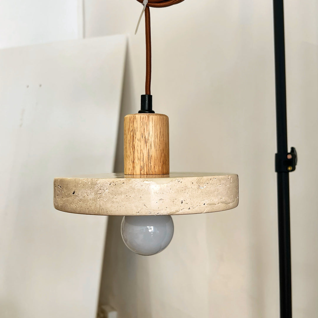 Suspension lumineuse en travertin et bois clair présentée sur support de studio pour mettre en valeur ses finitions.