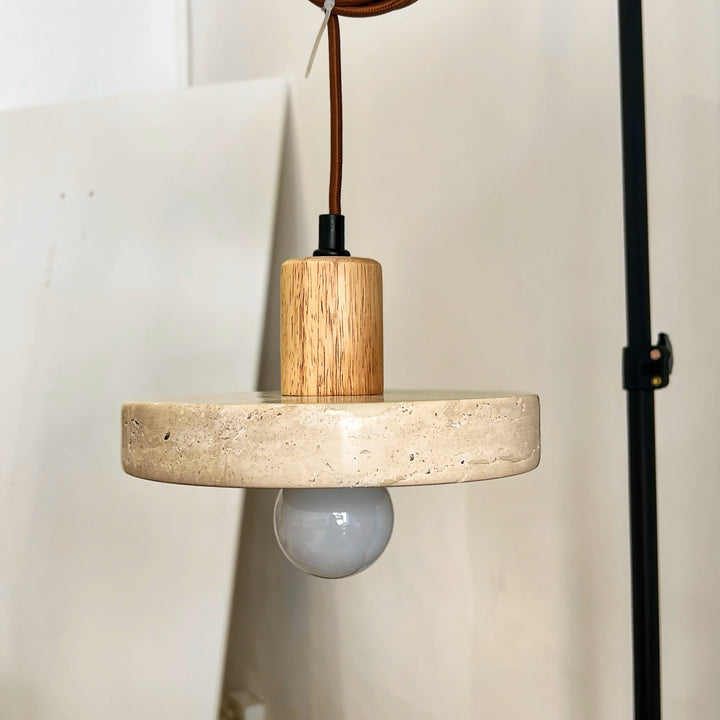 Suspension lumineuse en travertin et bois clair présentée sur support de studio pour mettre en valeur ses finitions.
