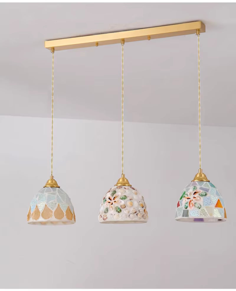 Suspension triple en verre façonné sur barre dorée, déclinant trois décors de coquillages dans un esprit côtier chic