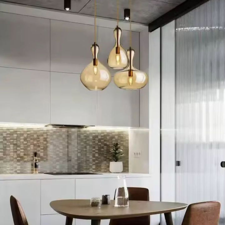 Au-dessus d'une table ronde, trois suspensions en verre ambré aux courbes organiques illuminent un espace repas contemporain.