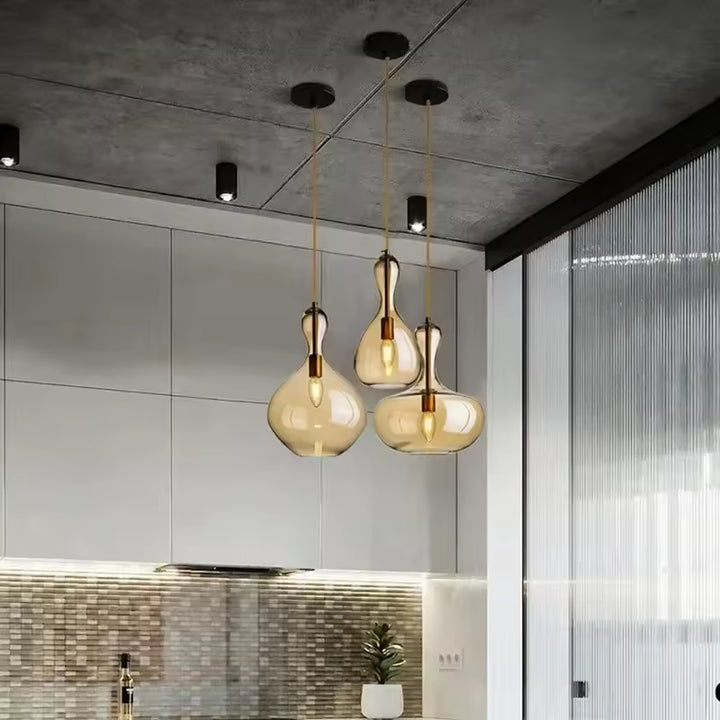 Trio de suspensions en verre ambré aux silhouettes fluides et sculpturales, éclairant une cuisine contemporaine.