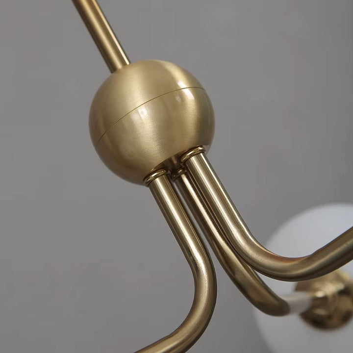 Gros plan sur les bras courbés en métal doré de la suspension tripode, inspirés du design italien vintage