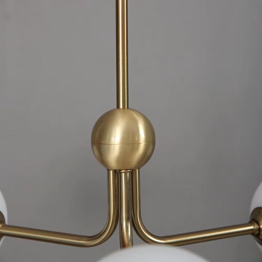 Détail de la structure dorée de la suspension tripode à globes opalins, aux lignes rétro et raffinées