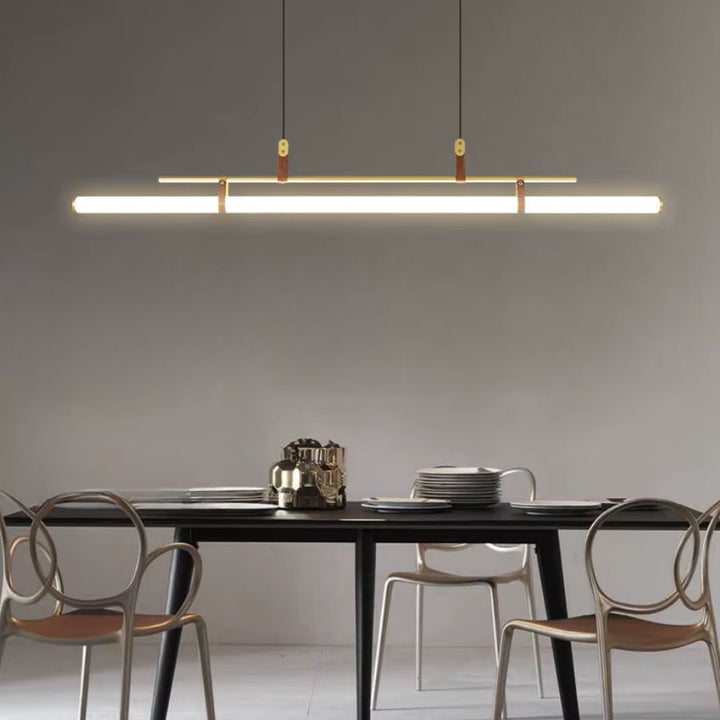 Ligne LED suspendue à structure dorée et attaches en cuir, mise en scène au-dessus d’une table au design épuré