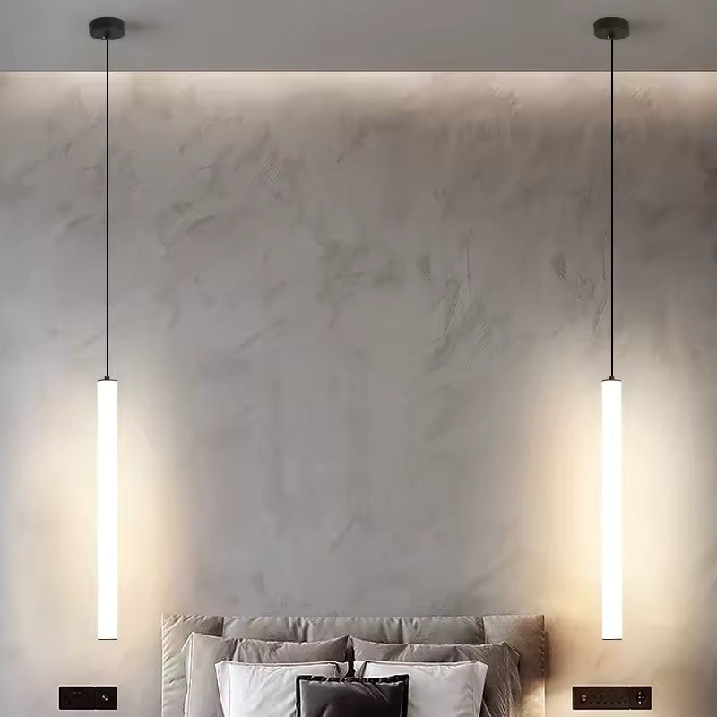 Deux suspensions tubes LED blancs verticaux éclairent les côtés d'un lit dans une chambre moderne au style minimaliste.