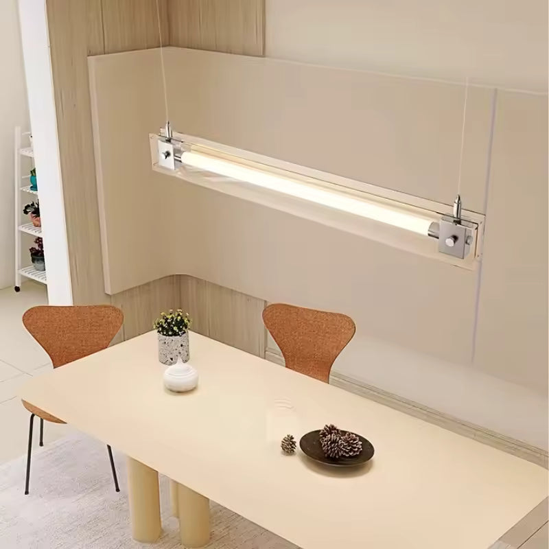 Suspension linéaire en verre transparent et acier inoxydable, éclairant une table dans un intérieur épuré