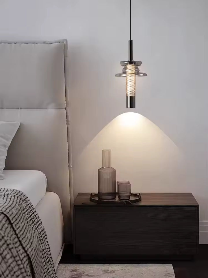 Au-dessus d’un chevet épuré, cette suspension tubulaire en verre fumé apporte une lumière douce et contemporaine