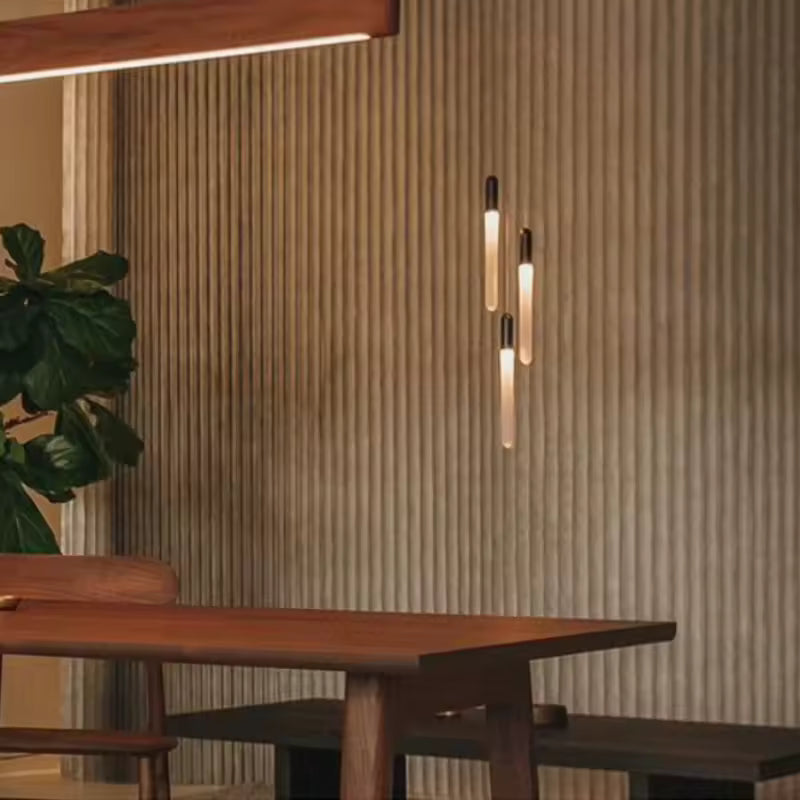 Près de la table, trois tubes lumineux élancés composent une suspension dorée au style chaleureux et contemporain