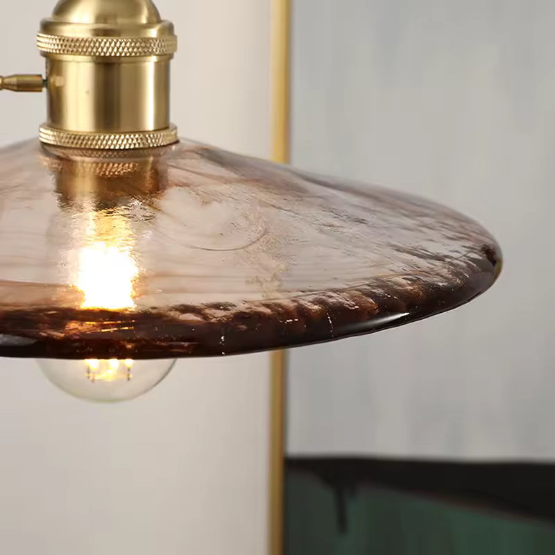Gros plan sur le verre ambré texturé et la douille en laiton d’une suspension au caractère vintage élégant