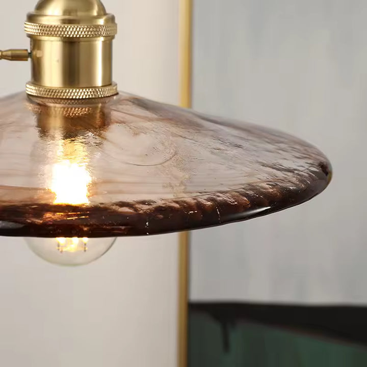 Gros plan sur le verre ambré texturé et la douille en laiton d’une suspension au caractère vintage élégant
