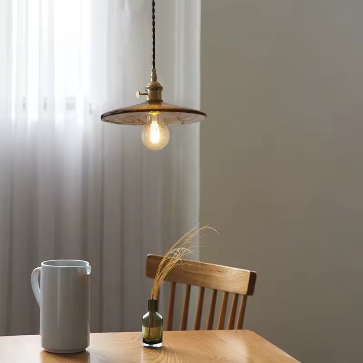 Luminaire suspendu en verre ambré texturé au-dessus d’une table, dans une ambiance vintage chaleureuse et naturelle