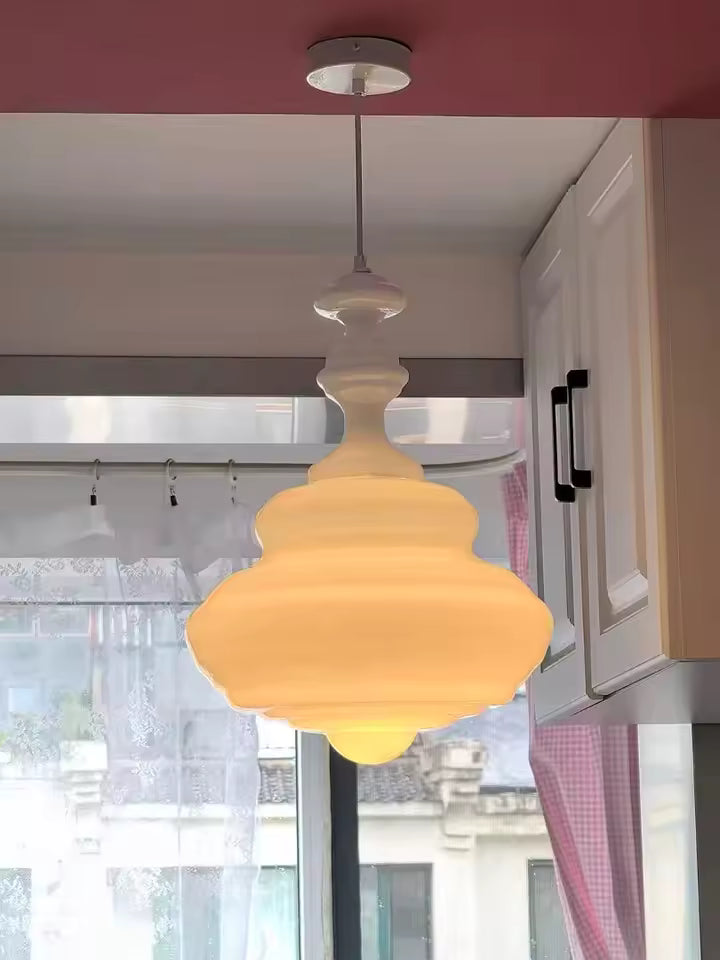 Suspension en verre blanc opalin aux courbes étagées, diffusant une lumière chaude dans une cuisine au charme rétro.
