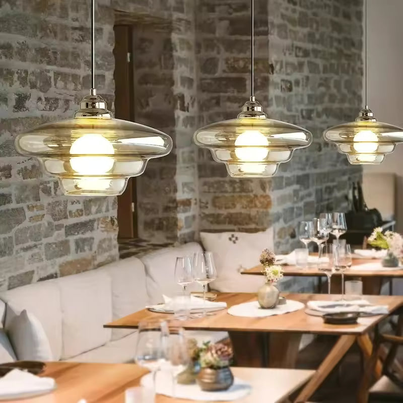 Trio de luminaires en verre champagne à silhouette étagée, suspendus au-dessus de tables de restaurant