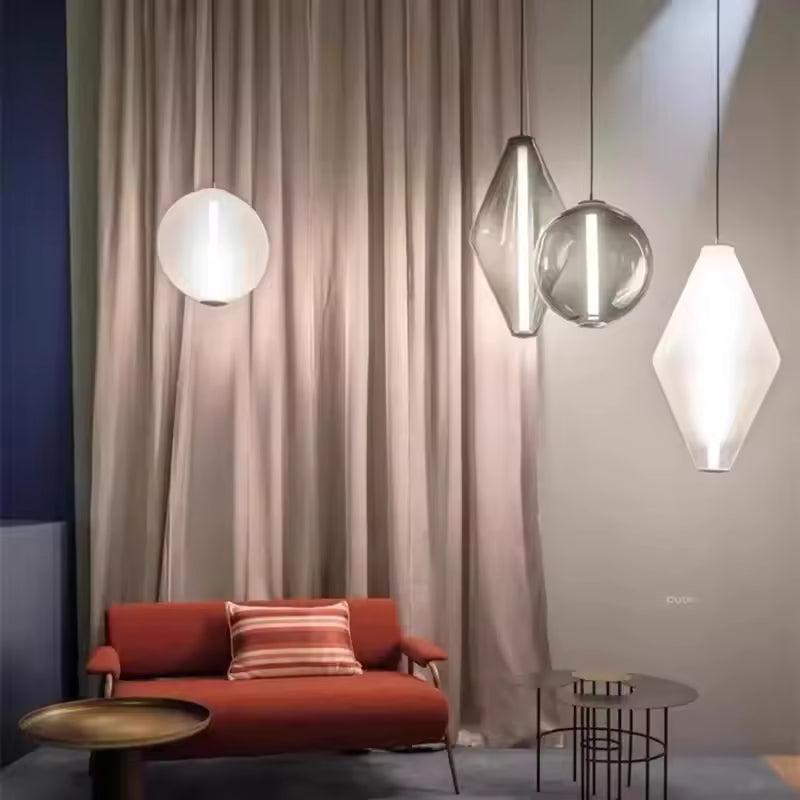 Lampes suspendues en verre aux silhouettes graphiques et contemporaines, mises en scène dans un salon élégant