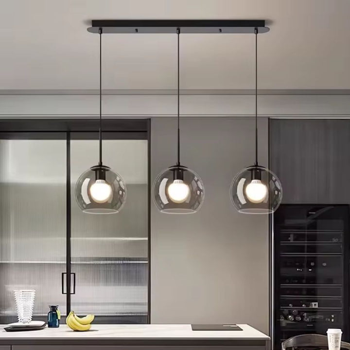 Au-dessus d’un îlot de cuisine, trois globes fumés composent un luminaire noir au style contemporain