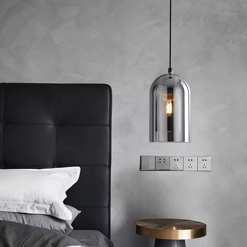 Au-dessus d'une table de chevet, une suspension en verre fumé aux reflets métallisés sublime une chambre au style industriel chic.