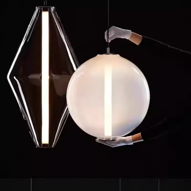 Deux lampes suspendues en verre, l’une géométrique et l’autre sphérique, traversées par une ligne lumineuse verticale