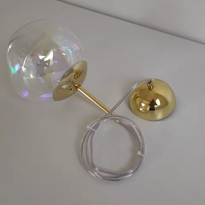 Détail d’une suspension en verre irisé avec monture dorée et câble réglable, au style chic et contemporain