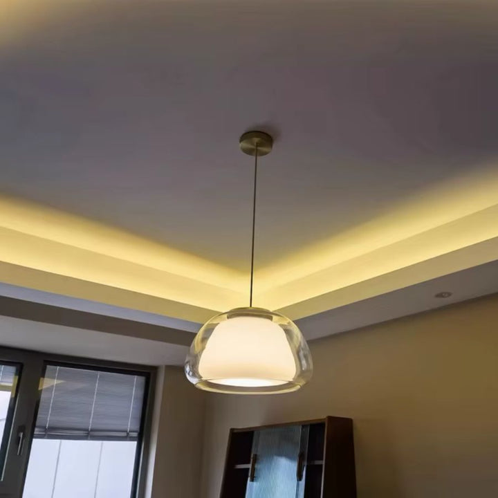 Luminaire suspendu en verre transparent et opalin, diffusant une lumière douce dans un intérieur contemporain