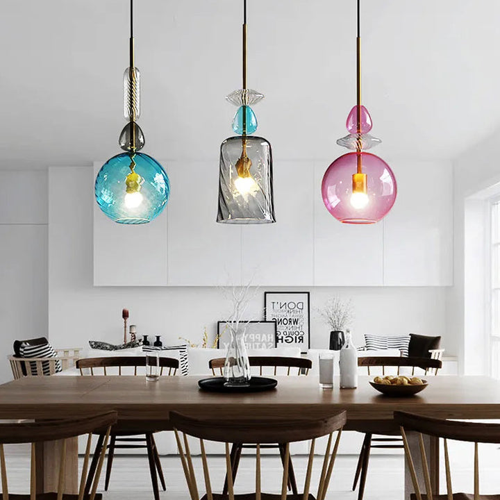 Trio de lampes suspensions en verre coloré murano au-dessus d'une table à manger dans une cuisine au style contemporain.