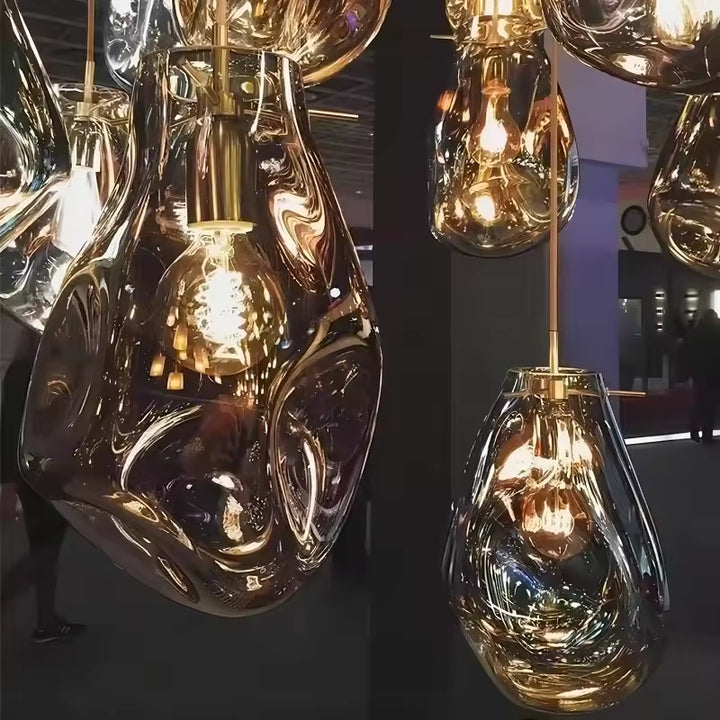 Gros plan sur des suspensions artistiques en verre soufflé aux courbes irrégulières, reflets dorés et ampoules apparentes.