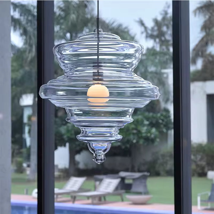 Devant une baie vitrée, suspension en verre transparent aux reliefs concentriques et silhouette sculpturale contemporaine.
