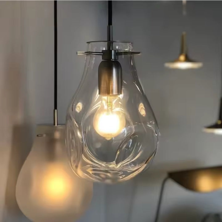 Gros plan sur deux suspensions en verre soufflé transparent et dépoli, aux courbes sculpturales et à la lumière chaude.