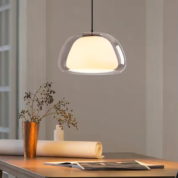 Luminaire suspendu en verre transparent avec cœur opalin, au style minimaliste et épuré au-dessus d’une table