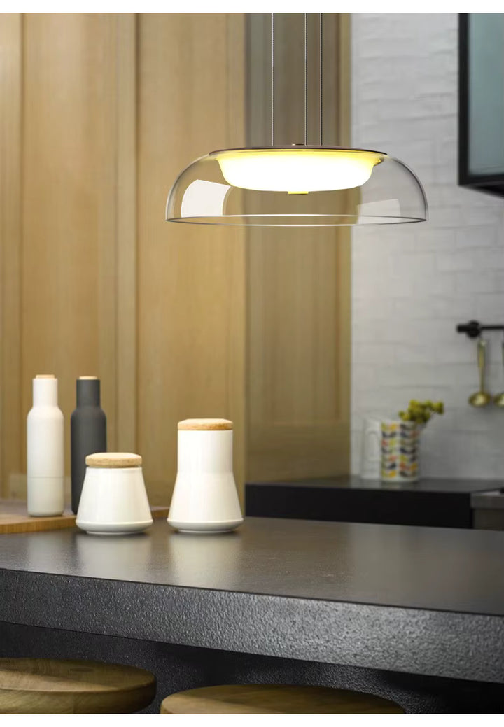 Au-dessus d’un îlot de cuisine, une suspension en verre transparent à diffuseur opalin apporte un style moderne et épuré