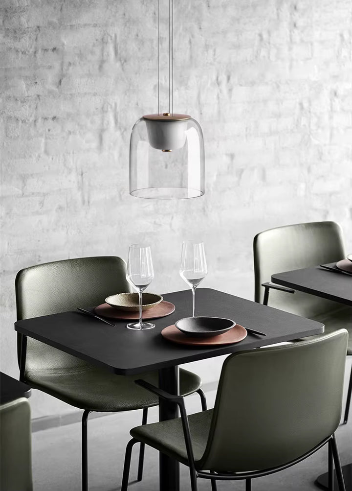 Au-dessus d’une table noire, une suspension en verre transparent à diffuseur opalin complète un décor design et contemporain