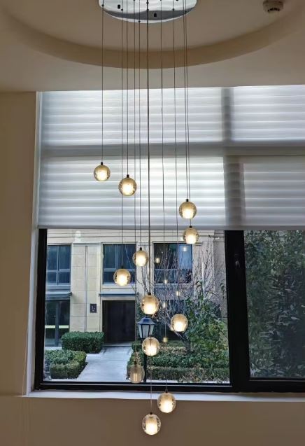 Suspension verticale de globes en verre lumineux devant baie vitrée, idéale pour entrée ou escalier moderne.