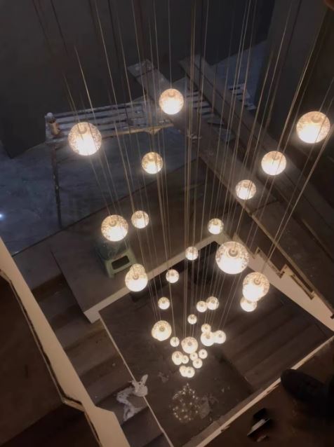 Suspension verticale de globes en verre illuminant la profondeur d’un escalier, éclairage design et ambiance chaleureuse.