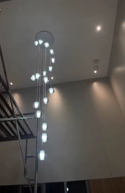 Suspension verticale multi-globes en verre pour hall à plafond très haut, éclairage design contemporain et aérien.
