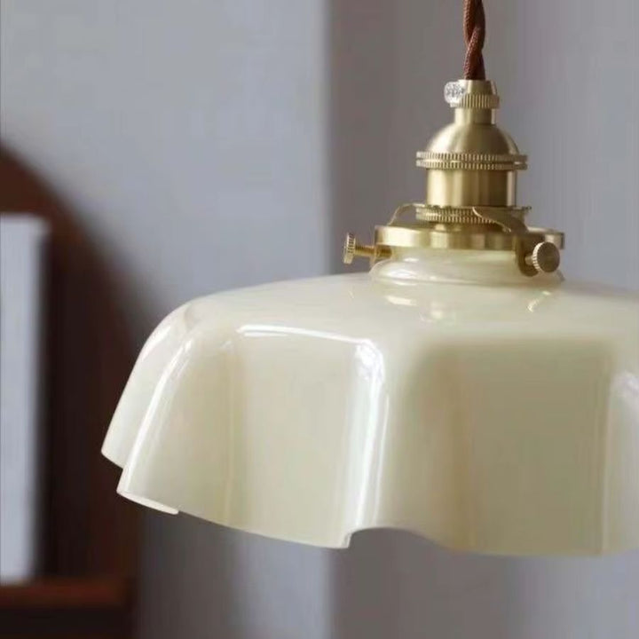Vue rapprochée d’une suspension beige à abat-jour festonné, ornée de détails en laiton au charme rétro élégant