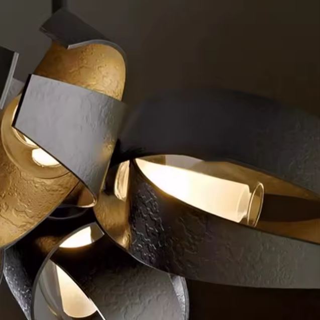 Détail des volutes en métal noir et doré d'une suspension sculpturale, aux textures martelées d'inspiration artisanale.