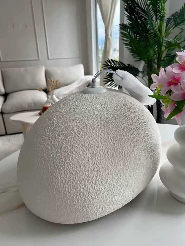 Gros plan sur le dôme asymétrique d'une suspension wabi-sabi blanche, à la surface granuleuse et au design sculptural.