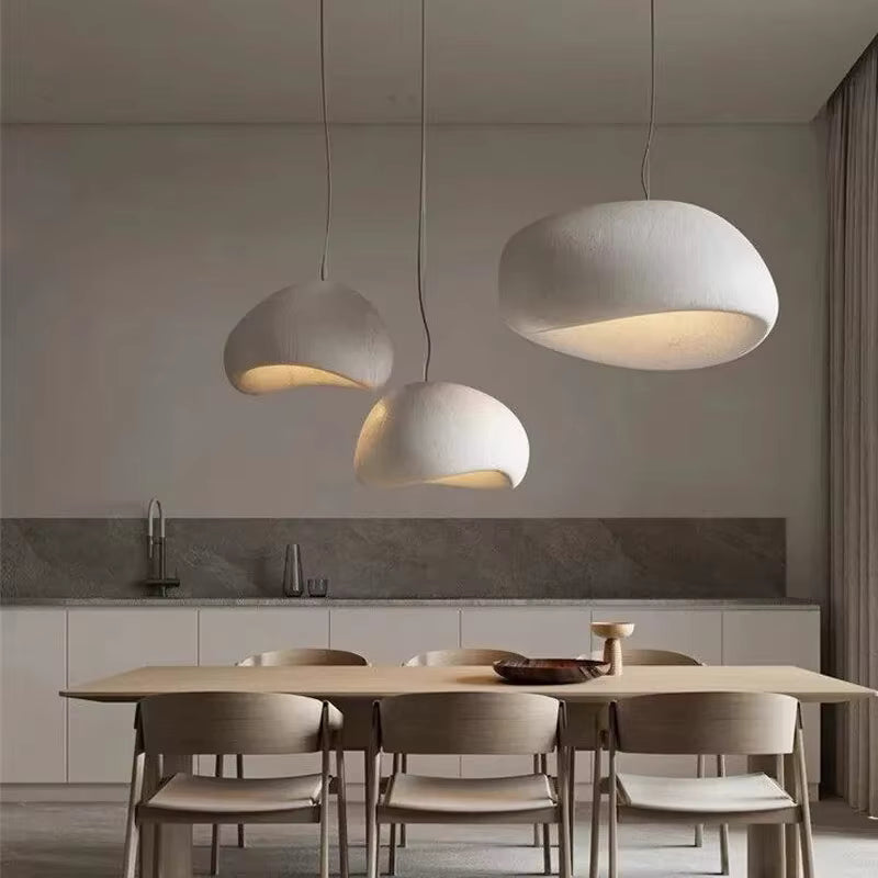 Trois suspensions blanches aux dômes asymétriques, d'inspiration wabi-sabi et organique, au-dessus d'une table à manger.