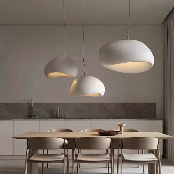 Trois suspensions blanches aux dômes asymétriques, d'inspiration wabi-sabi et organique, au-dessus d'une table à manger.