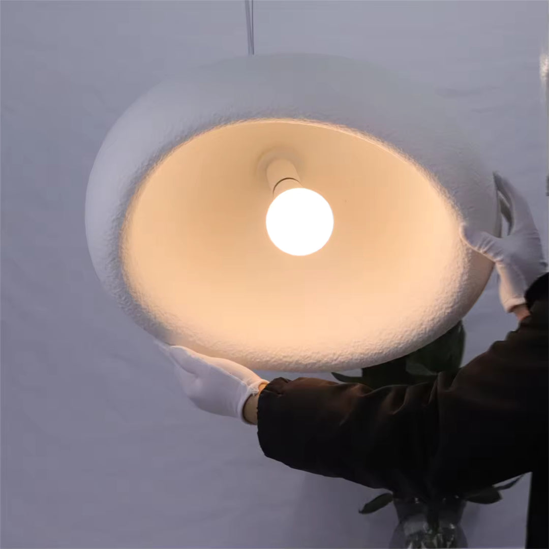 Vue de dessous d'une suspension wabi-sabi blanche à dôme texturé, révélant son ampoule et sa lumière chaude.