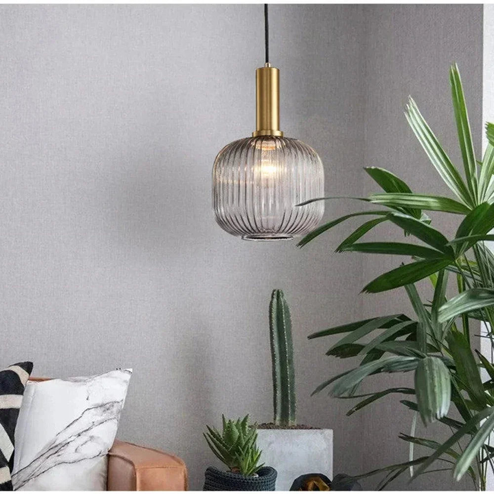 Suspension en verre cannelé dorée installée dans un coin de salon, à côté d’une plante fleurie décorative, apportant une lumière chaleureuse et une touche élégante à l’espace de vie
