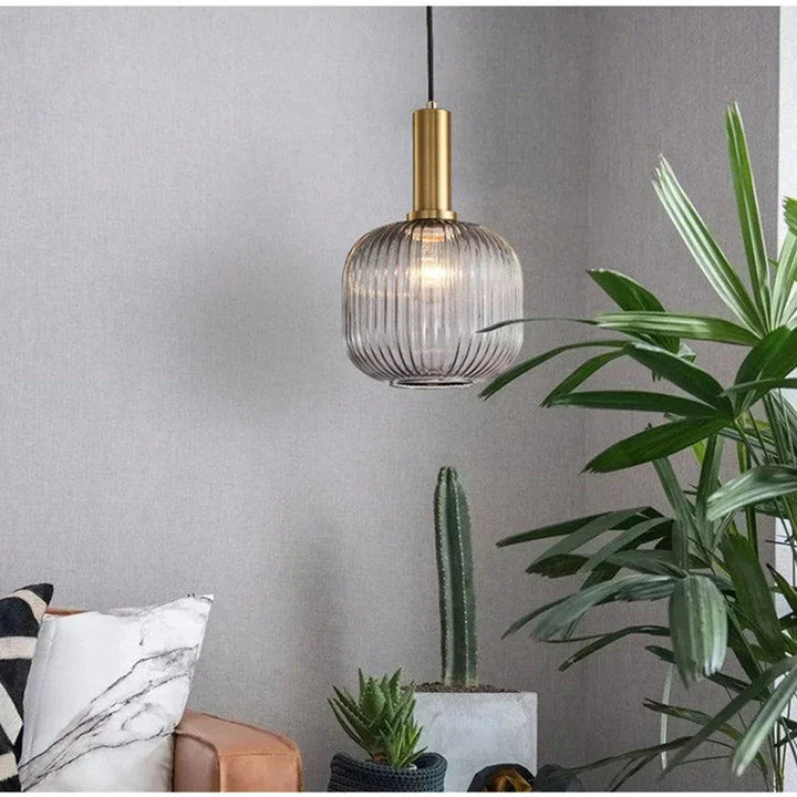 Suspension en verre cannelé dorée installée dans un coin de salon, à côté d’une plante fleurie décorative, apportant une lumière chaleureuse et une touche élégante à l’espace de vie