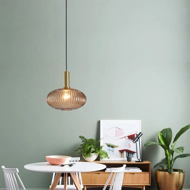 Suspension en verre cannelé dorée installée au-dessus d’une table dans une salle à manger moderne, accompagnée de plantes décoratives et de mobilier contemporain pour une ambiance chaleureuse et élégante