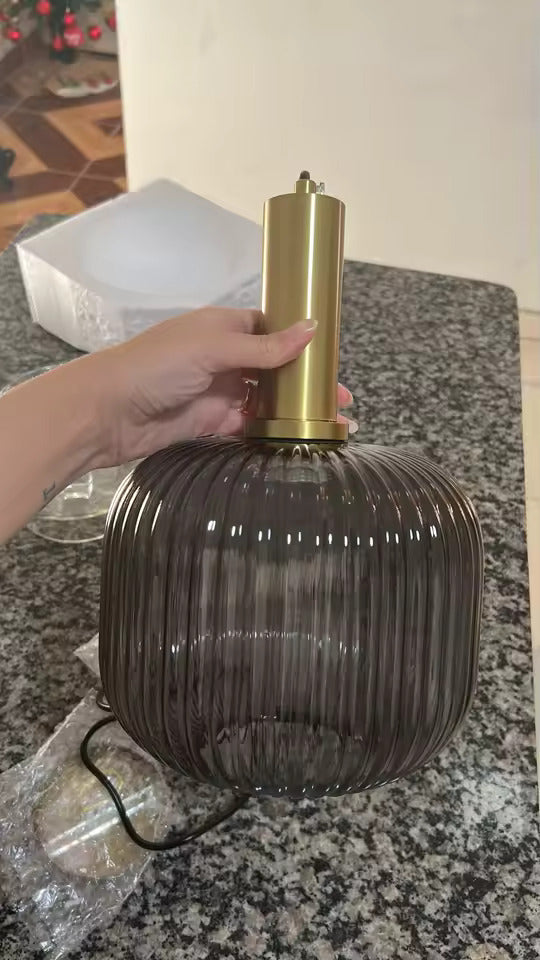 Suspension en verre cannelé fumé avec finition dorée, présentée en gros plan. Ce luminaire au design élégant associe un abat-jour en verre texturé à une structure métallique dorée pour une décoration intérieure raffinée.