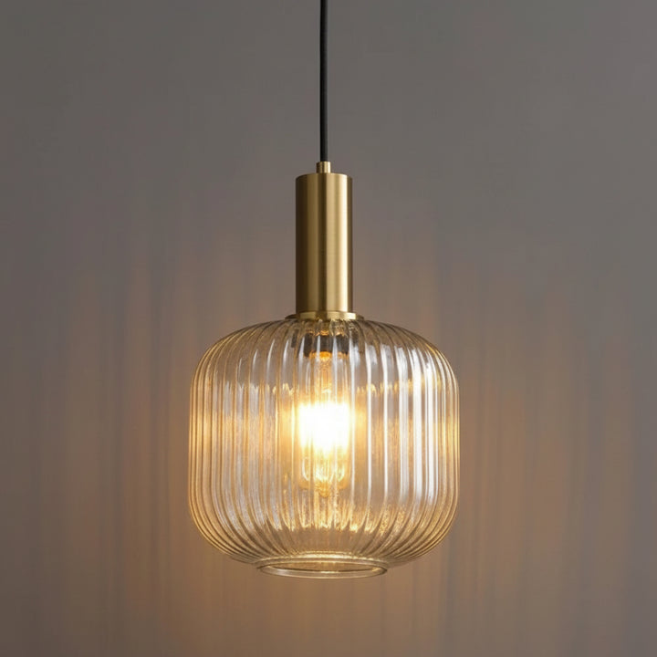 Suspension en verre cannelé transparent avec finition dorée, diffusant une lumière chaleureuse. Ce luminaire élégant apporte une touche raffinée et contemporaine à la décoration intérieure